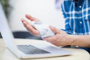Worker in office at laptop on desk holding hand in pain, wrist in brace for carpal tunnel symptoms 