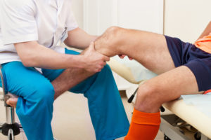 Doctor evaluating knee of soccer player in doctor’s office