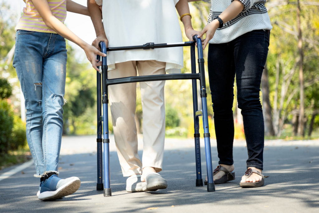Two people help an older person use a walker after hip surgery.