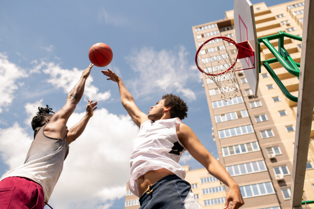 Two friends playing basketball outside of tall apartment complex.