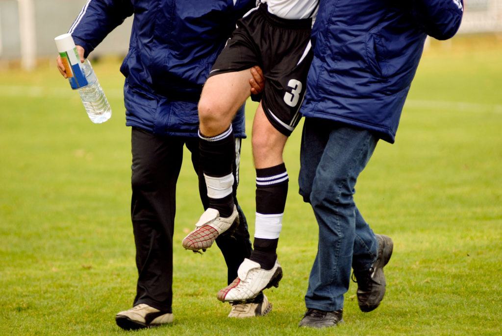 Two coaches carrying an injured soccer player off the field.