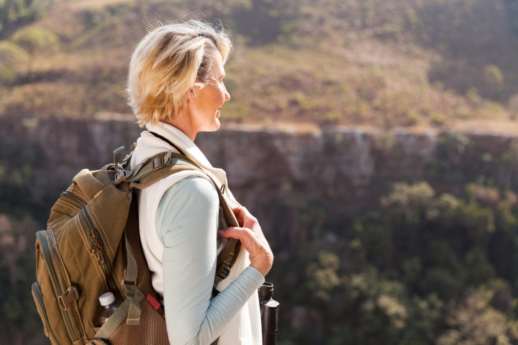  Middle-aged woman hiker wearing a backpack enjoys the outdoors and gazes out over a hilly area.