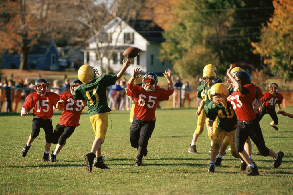 A young football player is rushed as he throws the ball during a game in a residential neighborhood.