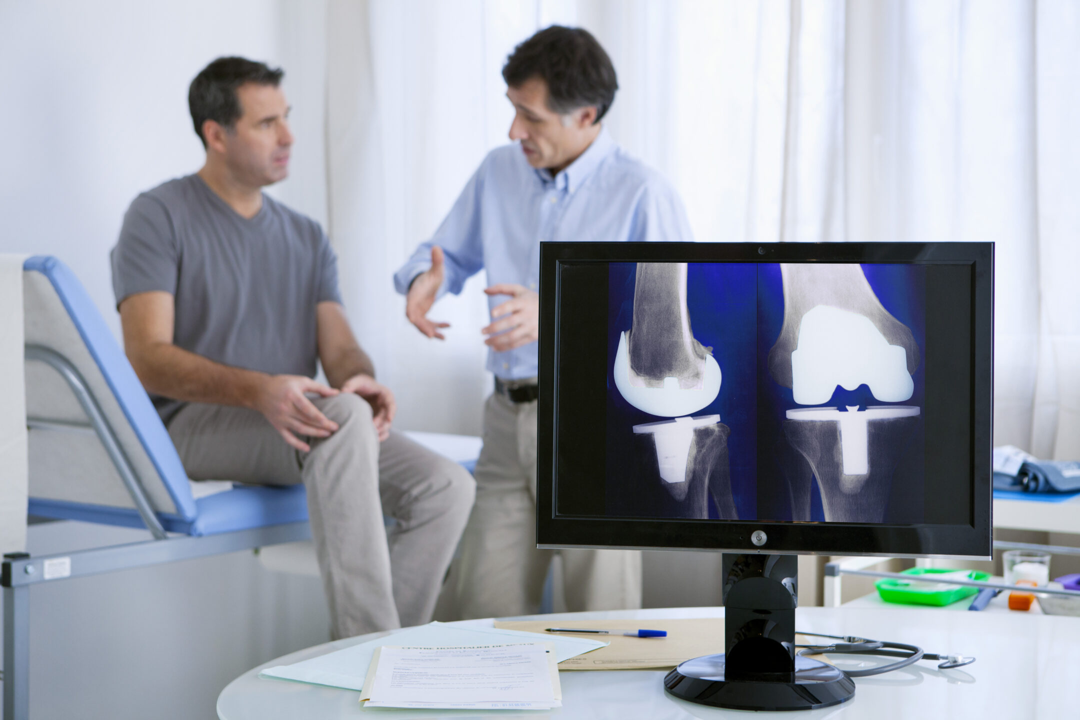 Orthopedic surgeon consults with a patient with a knee x-ray in the foreground. 