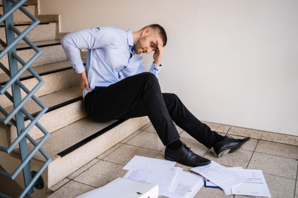 A man has an injury at work from a fall on steps and sits on them with scattered papers around him
